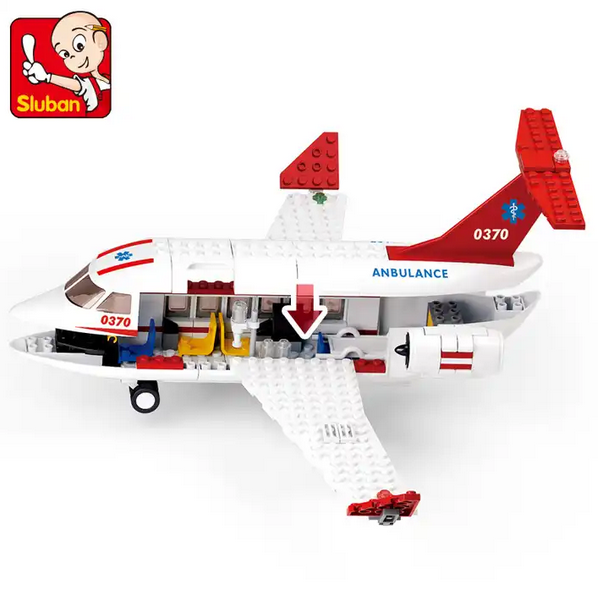 A toy medical emergency scene with a white airplane marked "Ambulance," several figures, and a small ambulance vehicle. Two figures carry a stretcher with a patient figure.